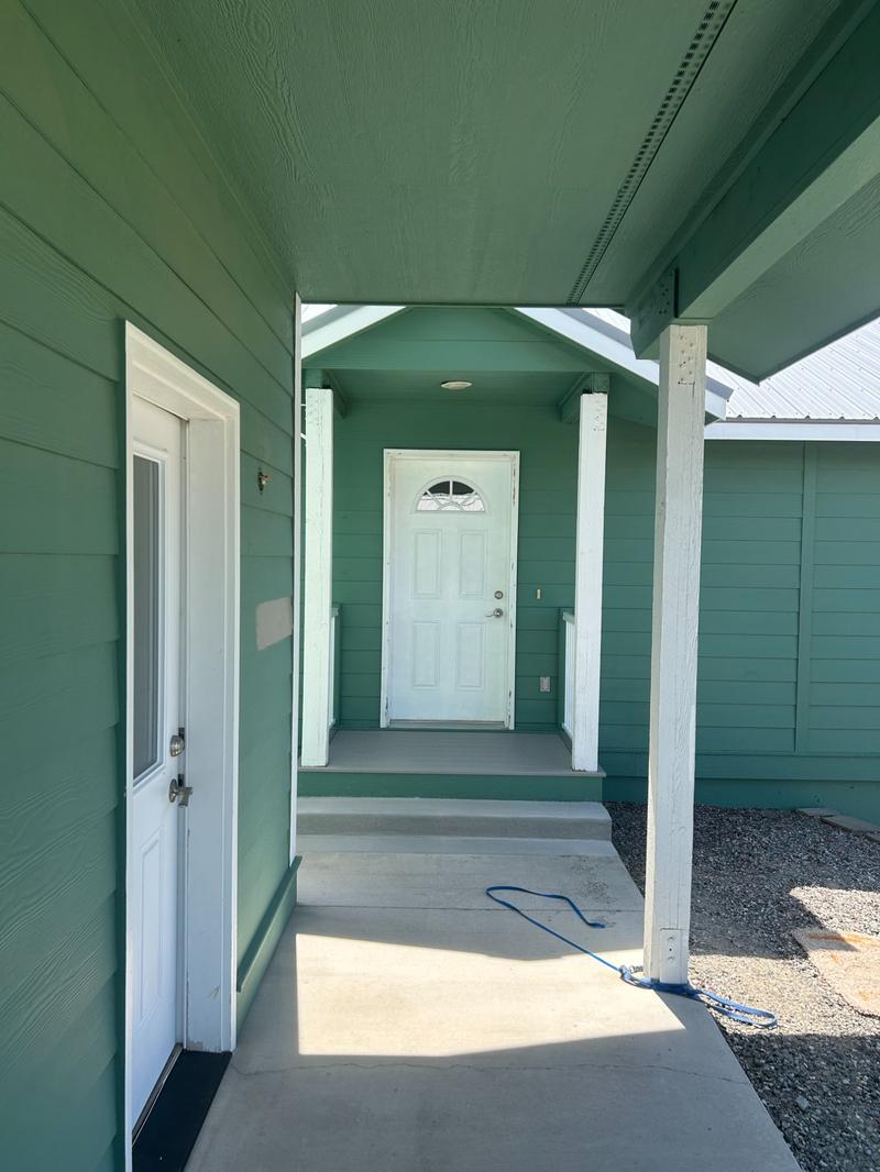 Covered breezeway between green painted buildings with white door and columns